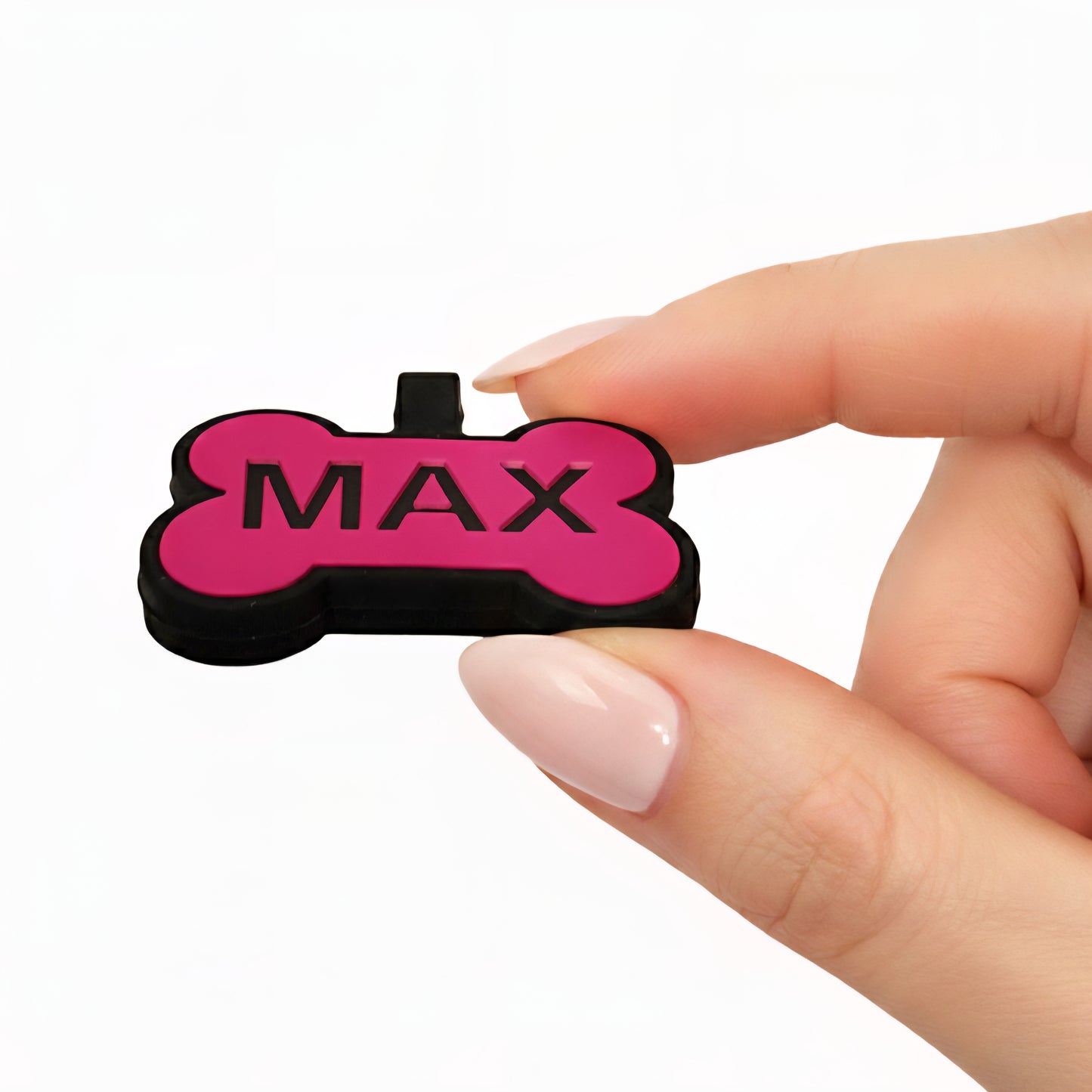 Pink and black bone-shaped pet tag with 'MAX' text held by a hand on a white background