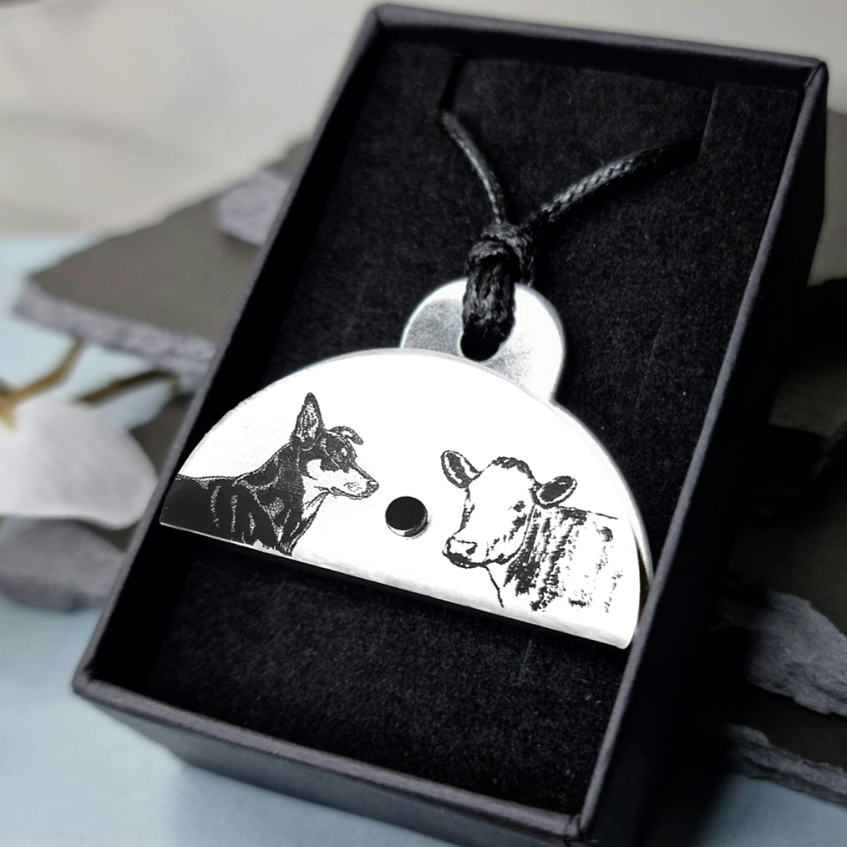 Stainless steel shepherds whistle pendant with engraved images of a cow and a kelpie dog in a black box.